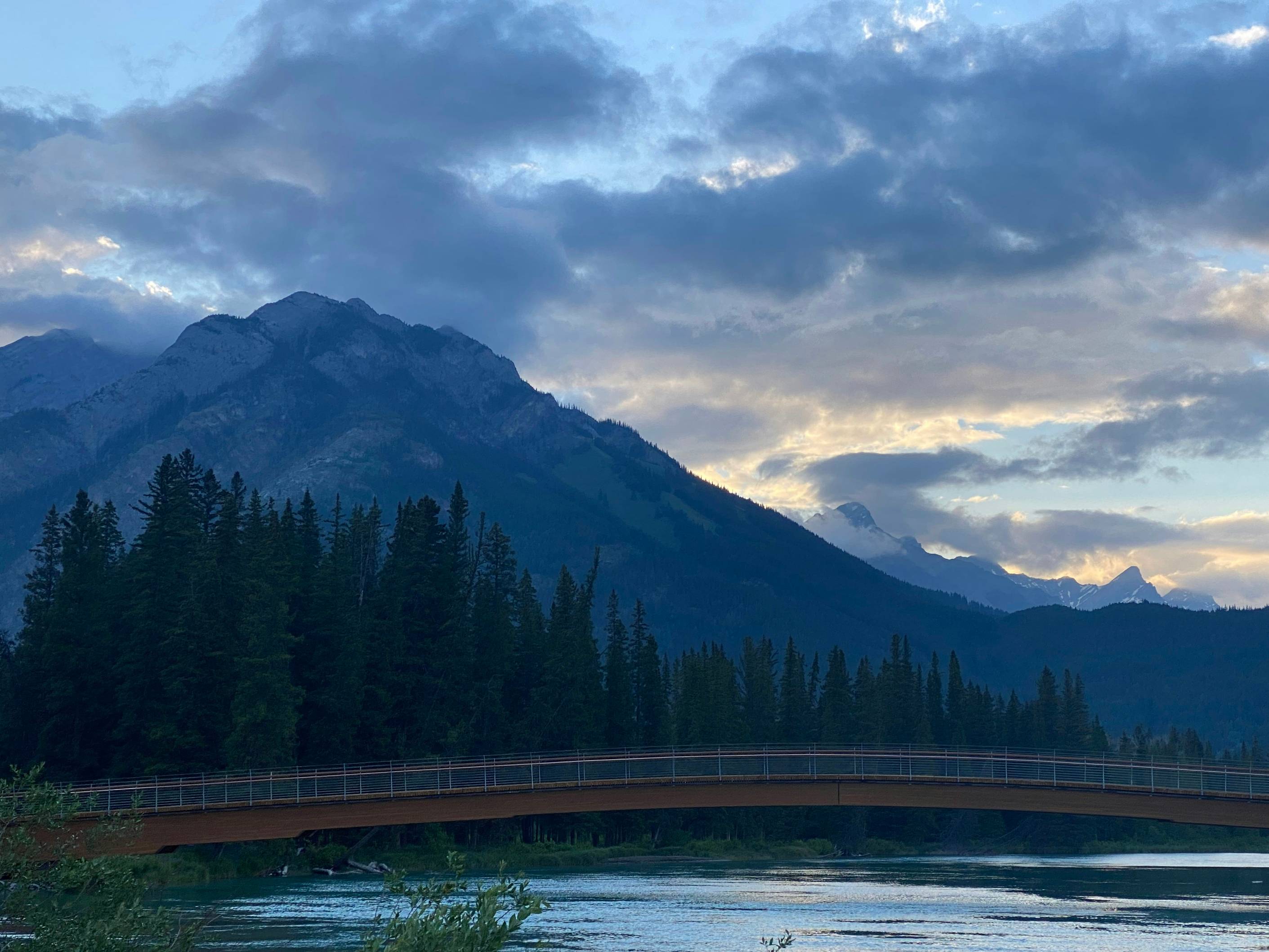 a bridge over a river with trees and mountains in the background