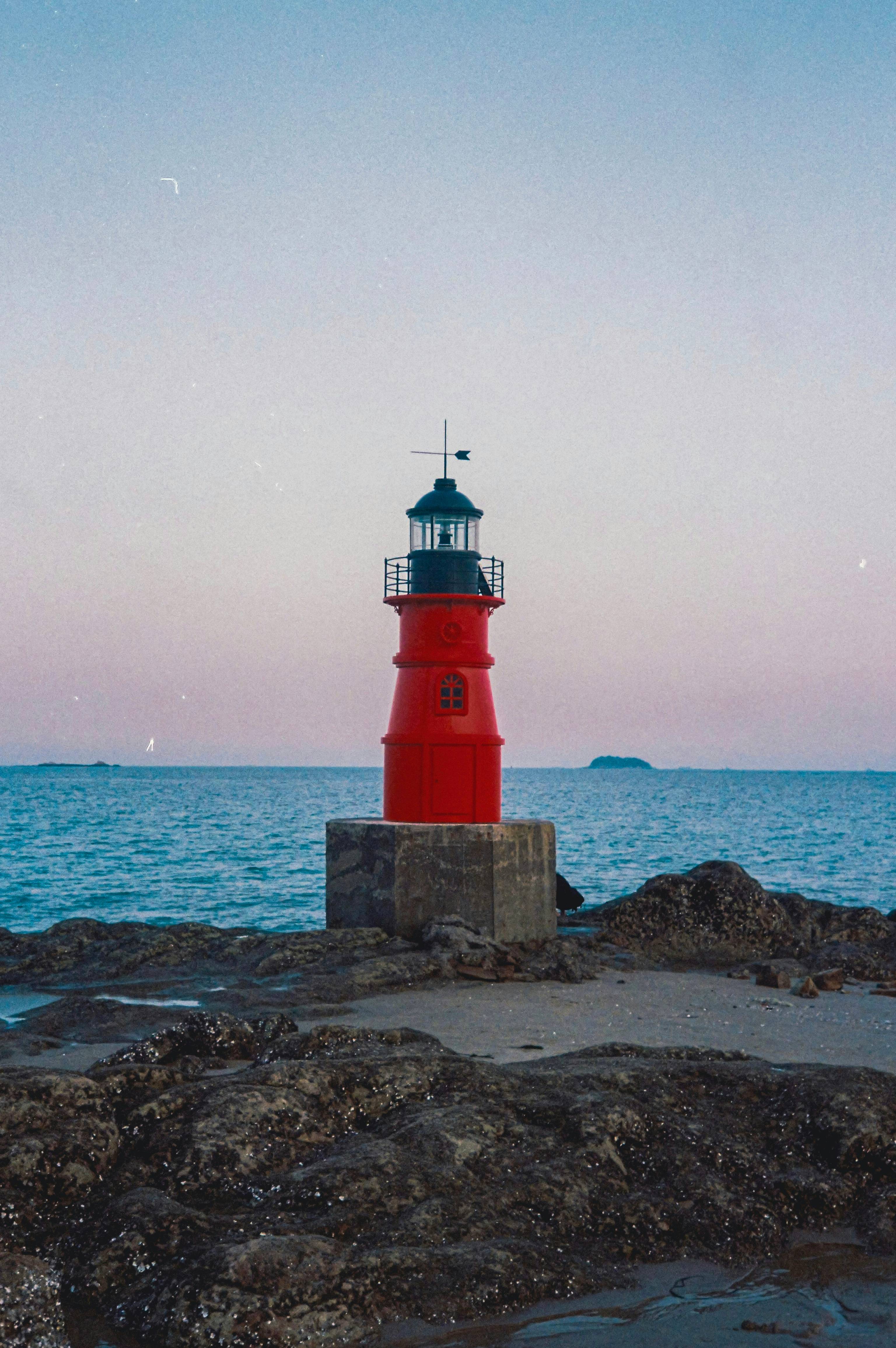 A red light house sitting on top of a rocky shore
