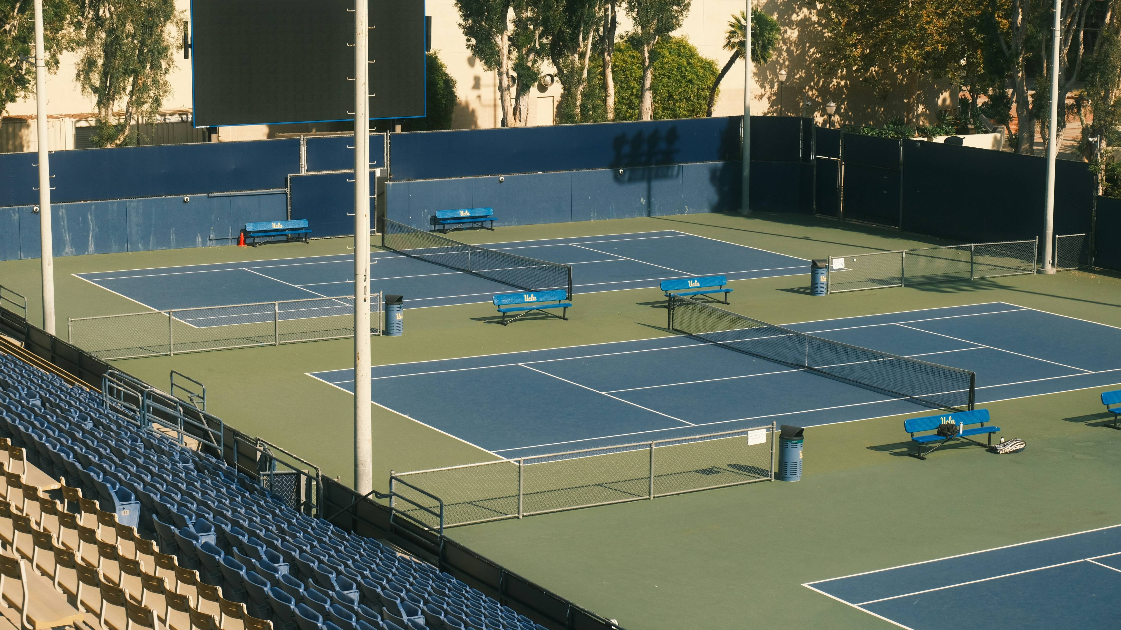 Empty tennis courts with blue seating and nets.