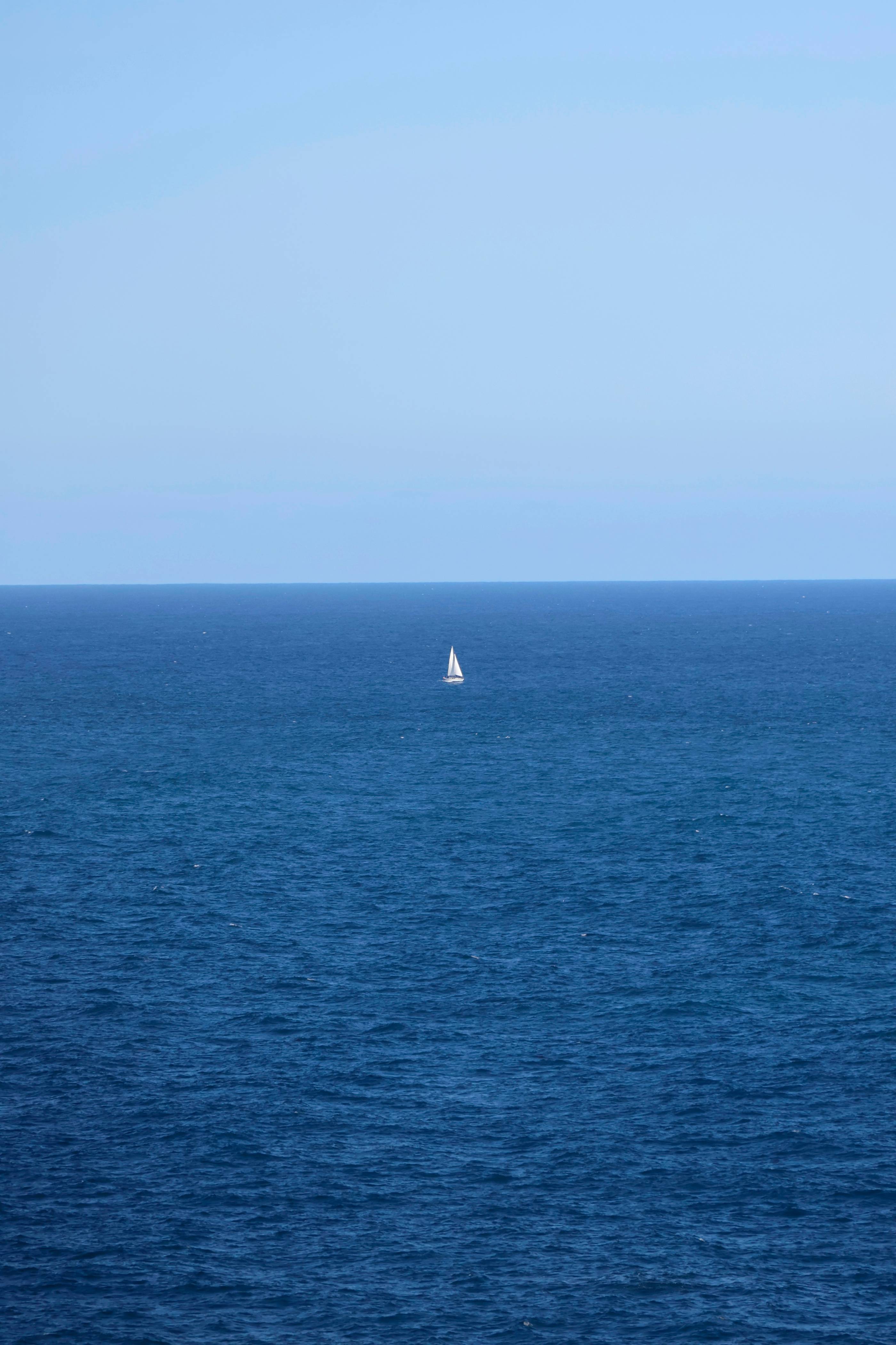 A small sailboat floats on the vast ocean.